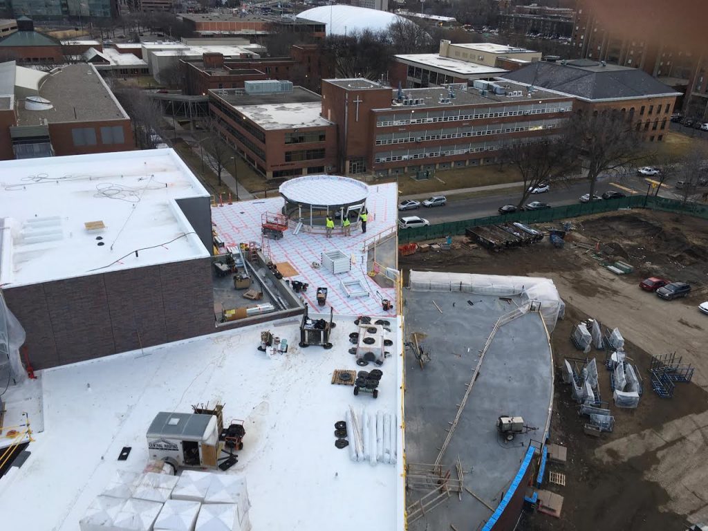 In this picture: [1] Crews install window frames on the circular structure extending above the ceiling of the suspended chapel. [2] The vapor barrier is complete on the lobby roof. [3] The base of the greenhouse can be seen to the left of the chapel. And [4] the flexible classroom roof, visible to the right, is being readied for the green roof to be installed in the summer.