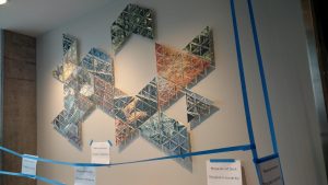 Multiple glass triangles installed in a geometric shape on a wall, with "So not touch" signs taped up all around