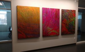 Three-piece art installation in oranges, pinks and reds, on a wall