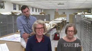 Three researchers seated in a long room with file cabinets and tables. 