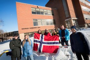 Students gathered on campus in the snow around a Norwegian flag