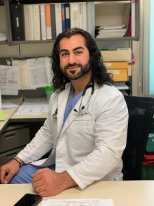 alum Hoshmand Las, PA-C sits in his white coat and scrubs in his office