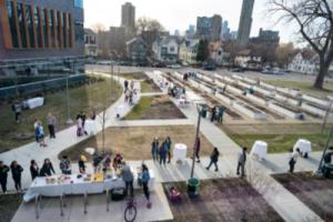 An aerial view of the Augsburg Community Garden. A table in the foreground has food on it, and people are lining up to serve themselves.