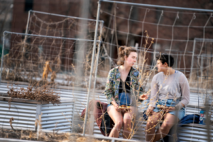 Two young people converse while sitting on the edge of a raised bed in the garden.